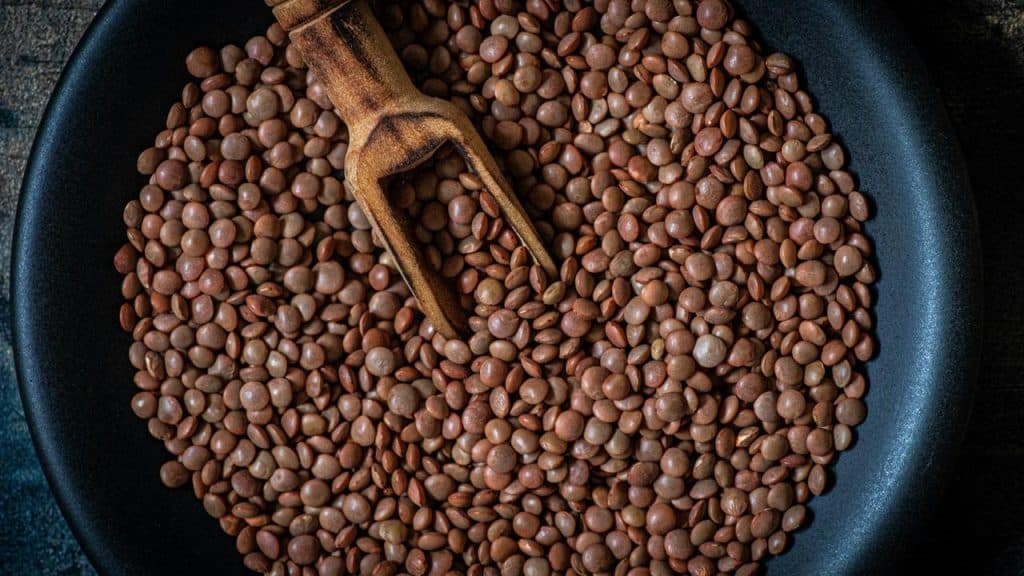 A pan of brown lentils with a wooden scoop.