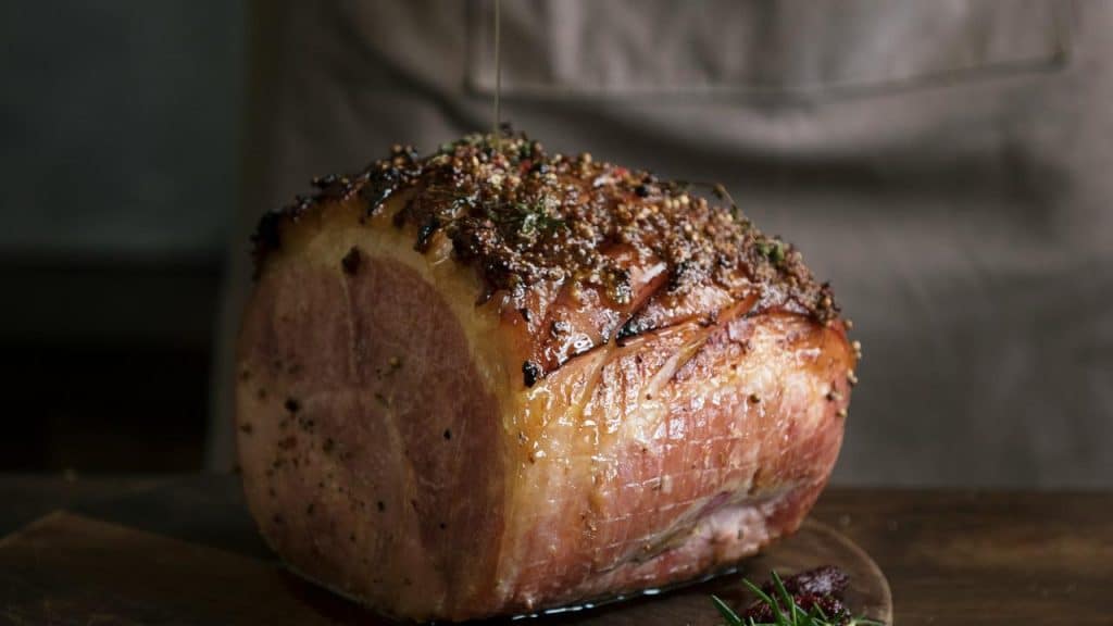 A glazed pork tenderloin on a cutting board being drizzled with glaze.