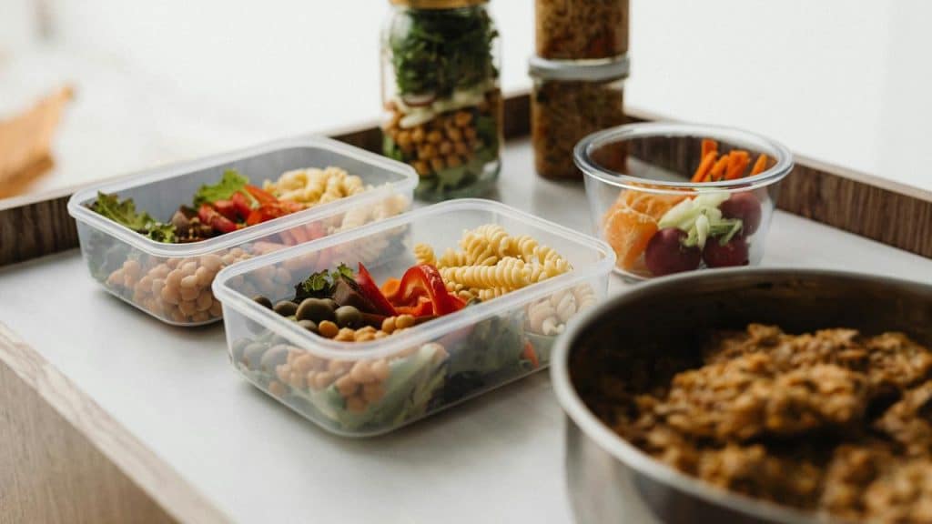A pair of meal prep containers filled with pasta, chickpeas, olives, and vegetables.