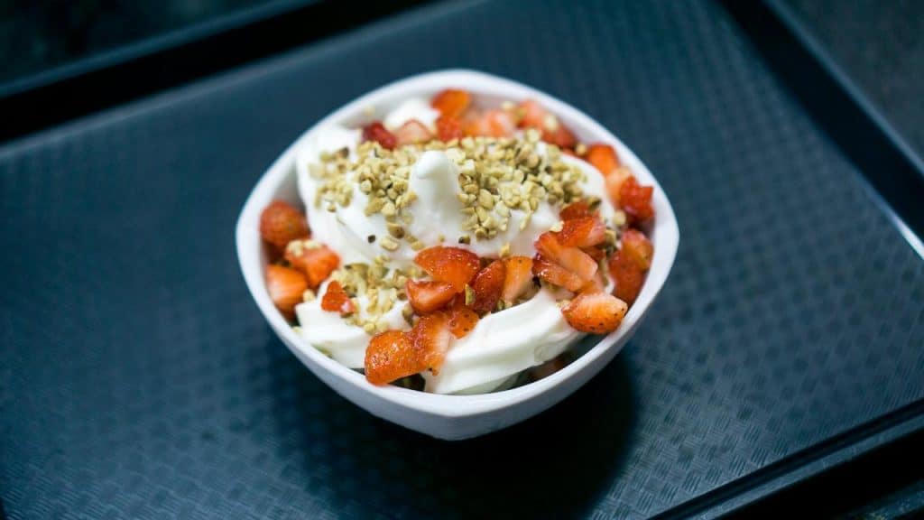 A bowl of soft-serve yogurt topped with chopped strawberries and crushed nuts.