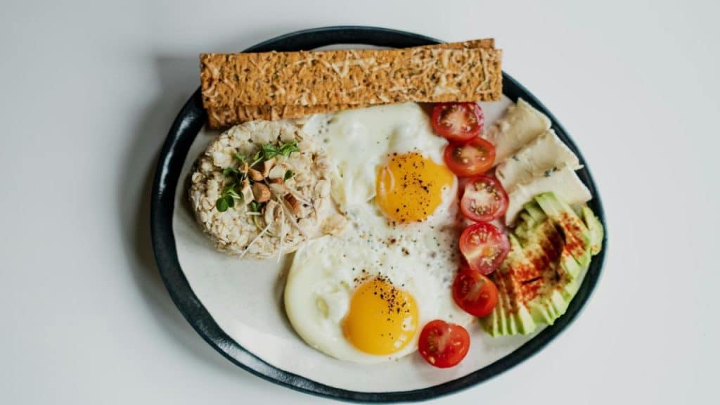 A plate of sunny-side-up eggs with avocado slices, cherry tomatoes, cheese, and a crispbread.