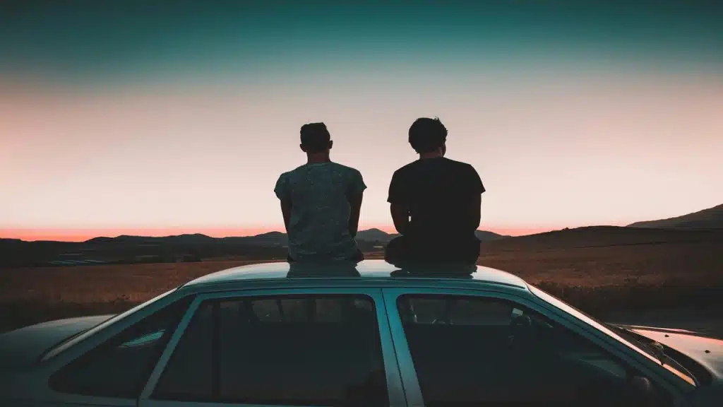 Two men sitting on the roof of a vehicle watching the sunset.