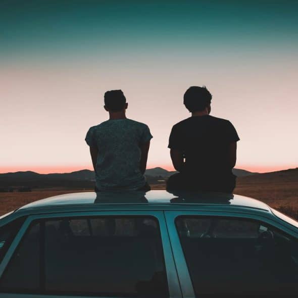 Two men sitting on the roof of a vehicle watching the sunset.