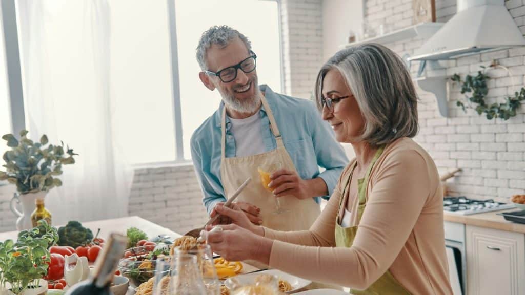 A happy older couple cooks together in a bright kitchen.