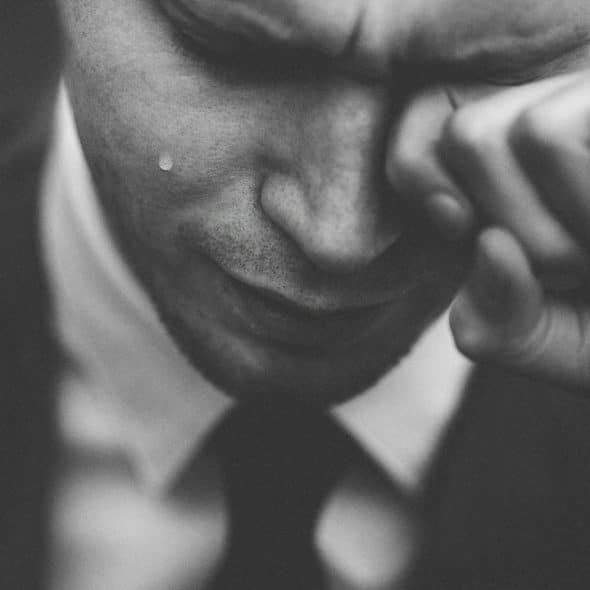 A grayscale close-up shows a man crying with a tear on his cheek.