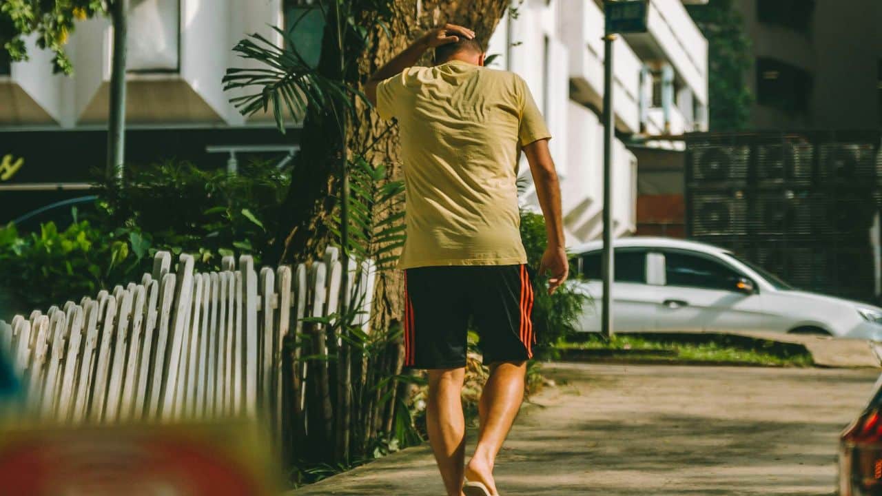 A man in a yellow shirt and black shorts walks away with his hand on his head.