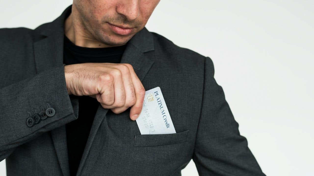 A man in a suit jacket is putting a "Platinum Credit" card into his pocket.
