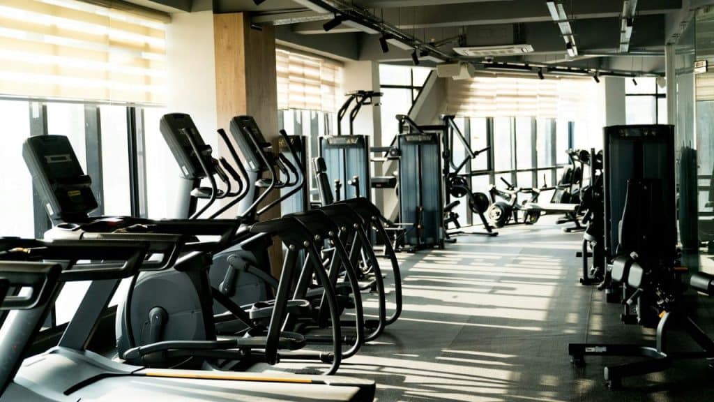 An empty gym with various exercise machines and large windows.