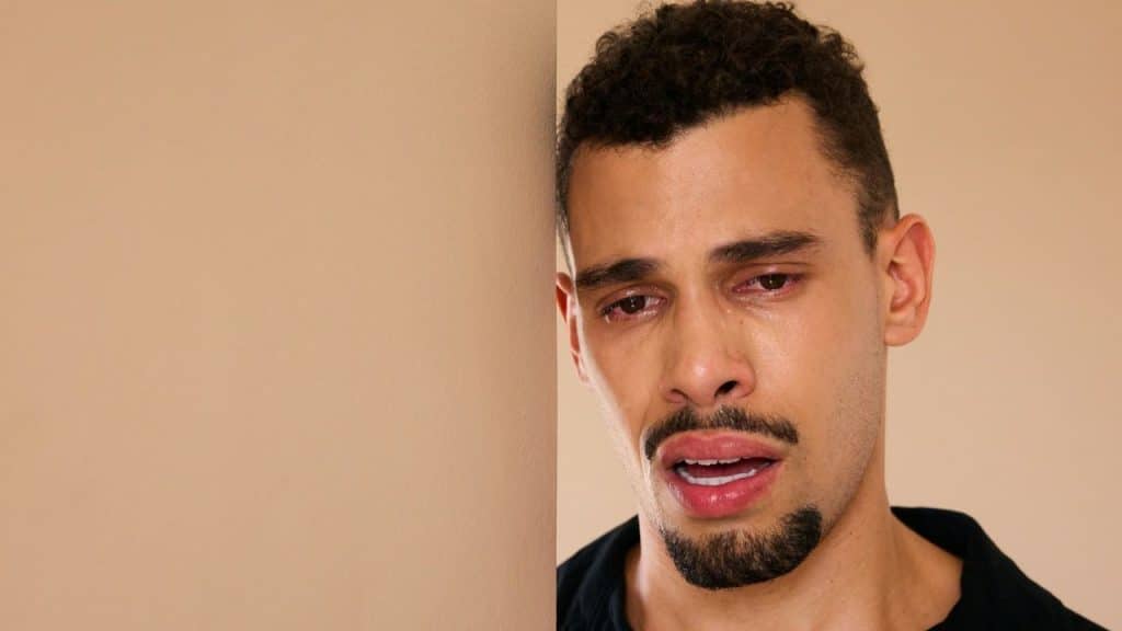 A man with a goatee and mustache cries, his face glistening with tears.