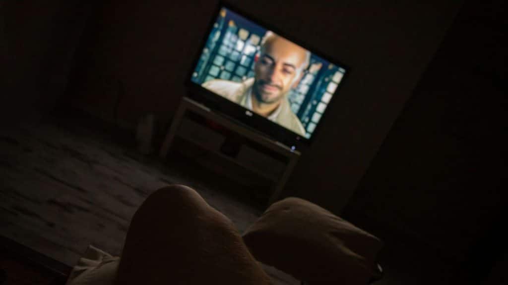 A television shows a man's face in a dark room, viewed from a low angle.