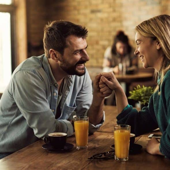 A smiling man and woman hold hands across a table with drinks in a cafe.
