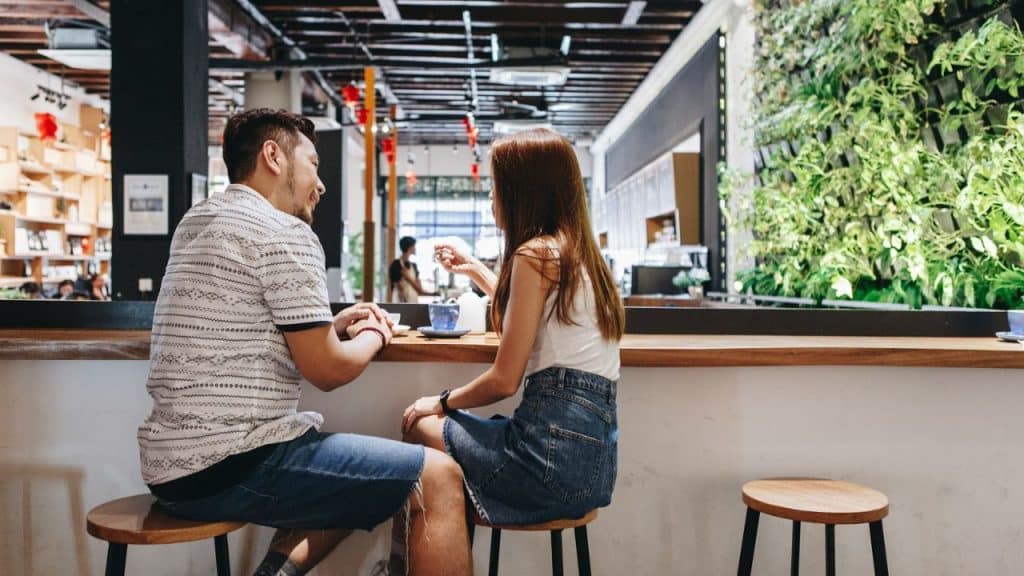 A man and a woman sit facing each other at a cafe counter.