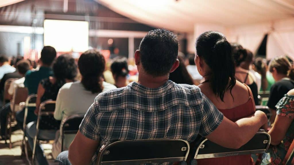 A man with his arm around a woman watches a screen in an outdoor event.