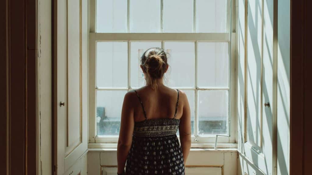 A smiling blonde woman vacuums a light-colored floor in a modern kitchen.