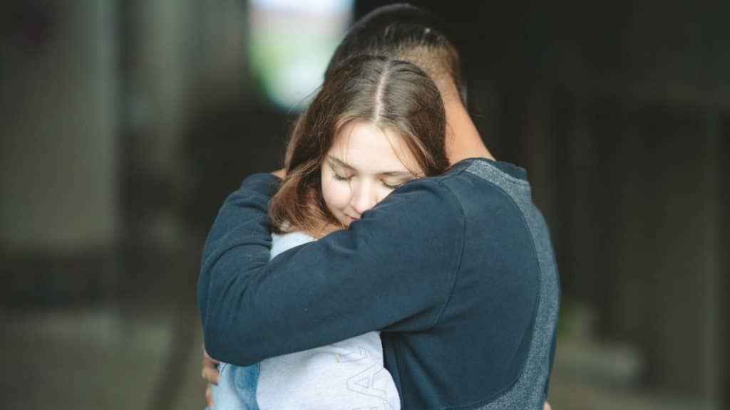 A woman with closed eyes is embraced by a man, with her head resting on his shoulder.