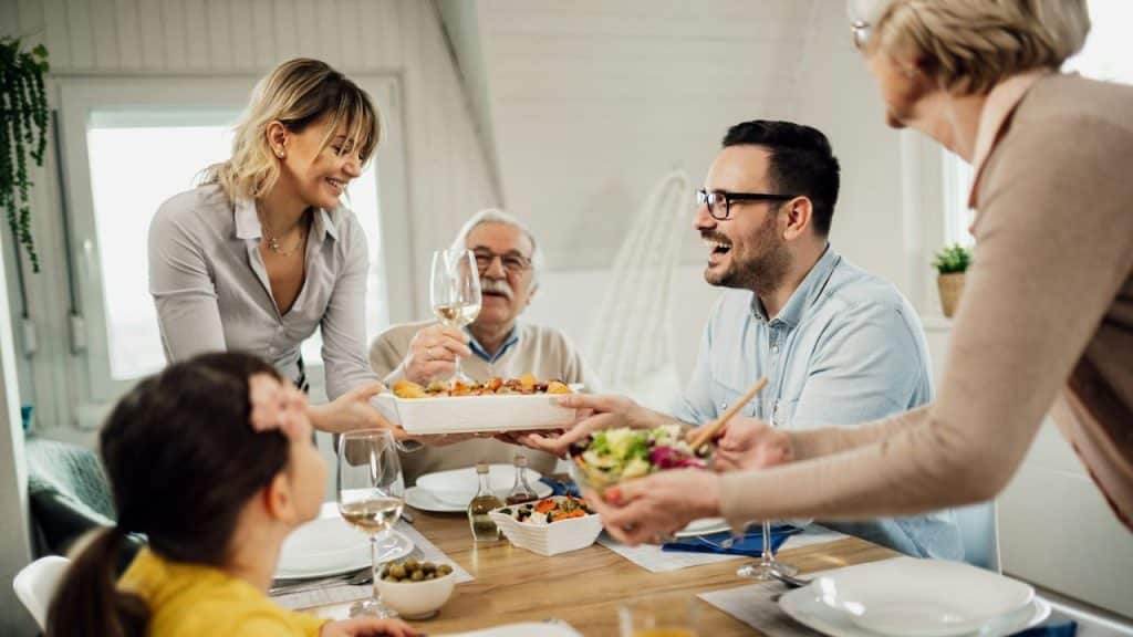 A family is gathered around a table, sharing food and drinks, with smiling faces.