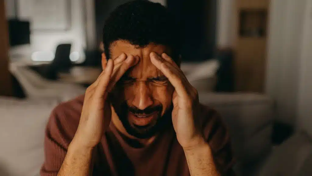 A distressed man with his eyes closed holds his hands to his temples, grimacing.
