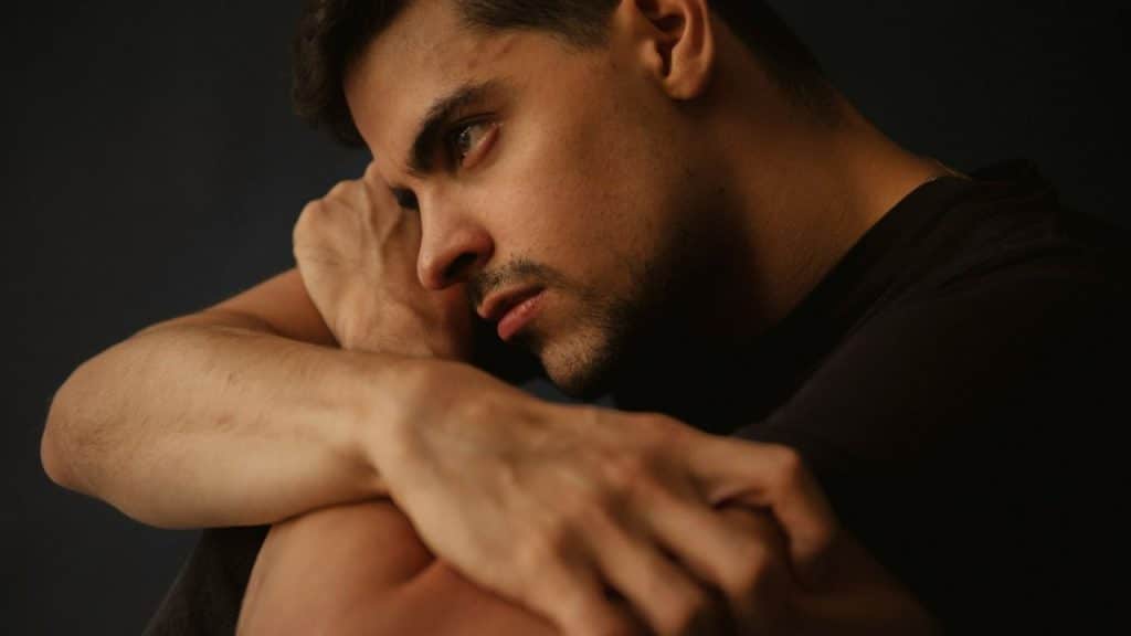 A man with a pensive expression looks off to the side, his hands near his face.