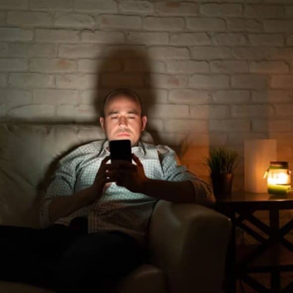 A man sitting alone at night, looking at his phone screen with a bittersweet expression.