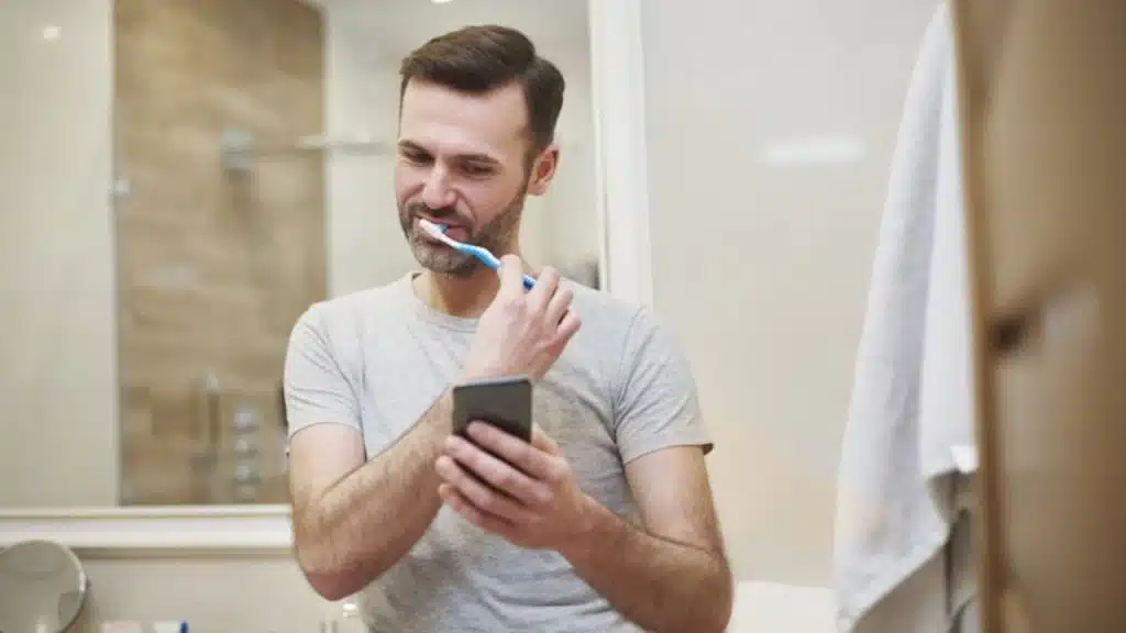 Man brushing teeth while on a video call with partner doing the same.