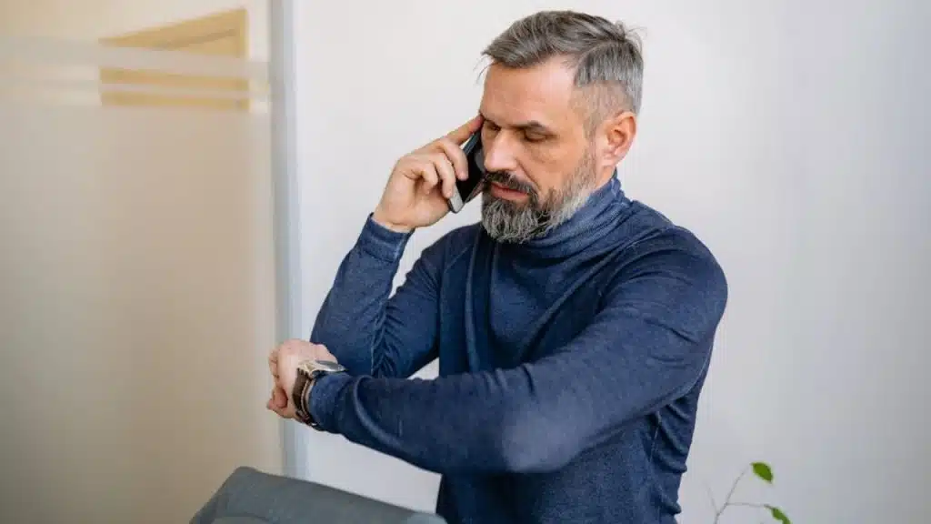 Man checking the time on his watch while talking with someone on the phone.