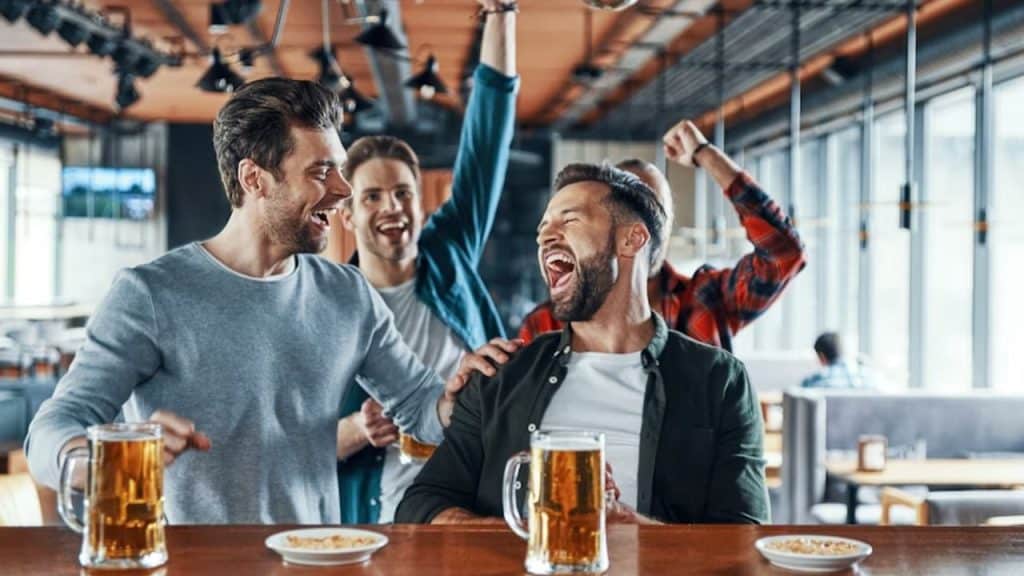 Man laughing while coworkers tease him at a bar.