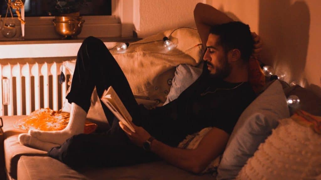 Man relaxing at home with book, enjoying time alone and away from the bar scene.