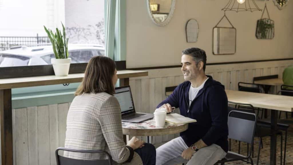 Couple having a sincere conversation at a cafe with an open laptop.