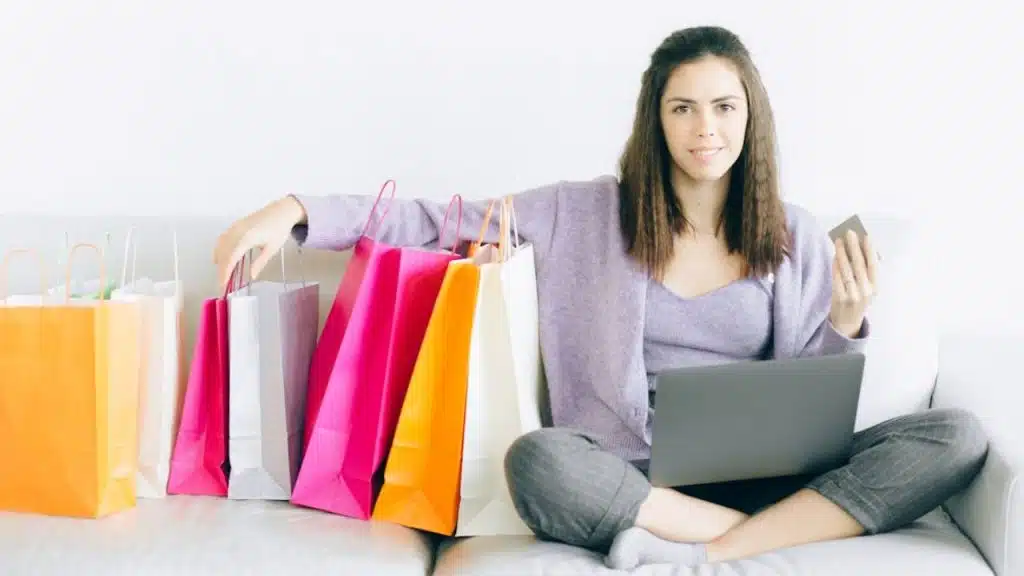 Woman smiling while sitting on the couch with shopping bags and credit card.