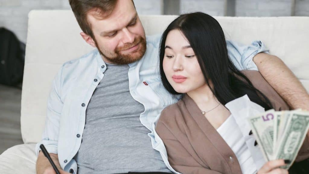 Couple sitting on the sofa working together on a savings goal list on a paper.