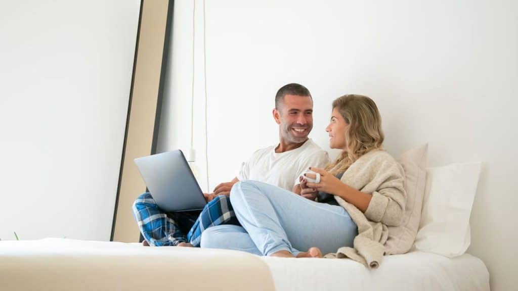 Couple smiling while discussing finances over coffee on the bed.