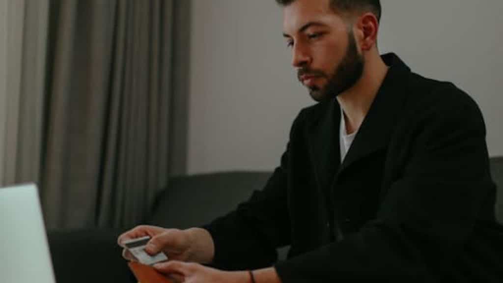 Man managing separate accounts on laptop while holding cards.
