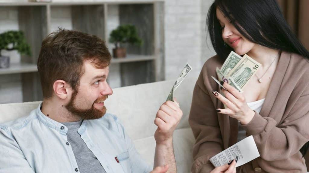 Supportive couple holding money while discussing finances calmly.