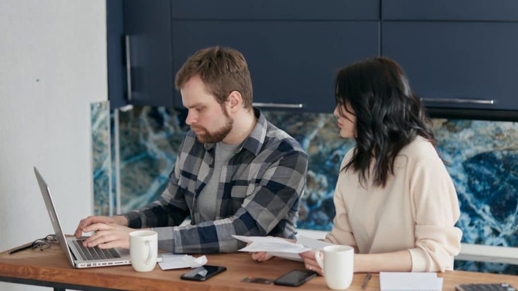 Man calculating finances carefully using a laptop while his partner is watching.