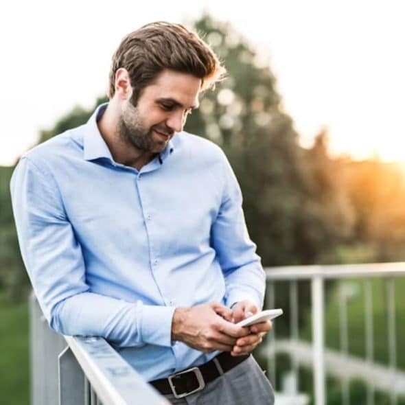 Man leaning on a railing with a phone on his hand and smiling.