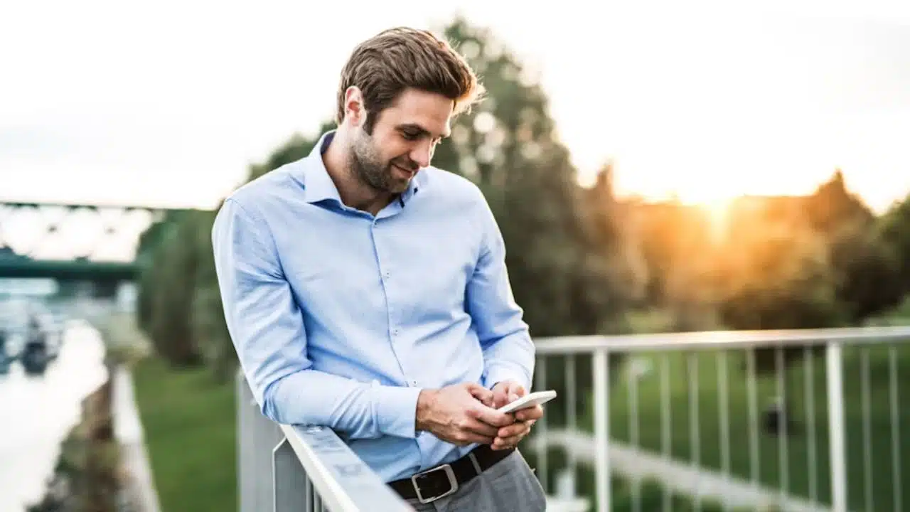 Man leaning on a railing with a phone on his hand and smiling.