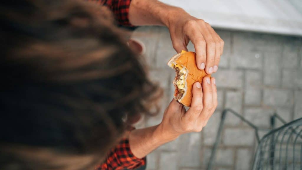 A person with curly hair and a plaid shirt holds a half-eaten burger, viewed from above.