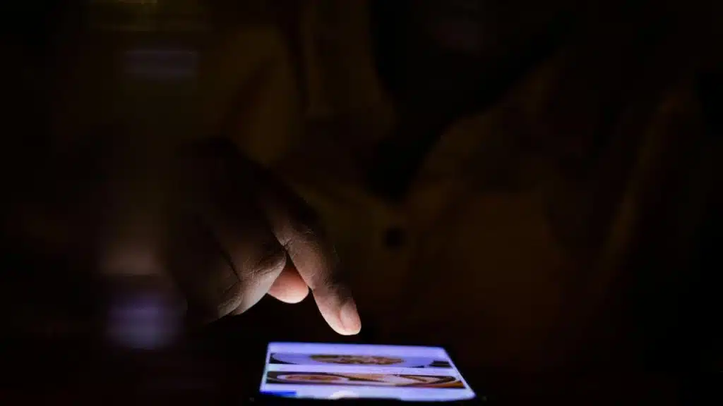 A hand tapping on a smartphone screen in the dark.