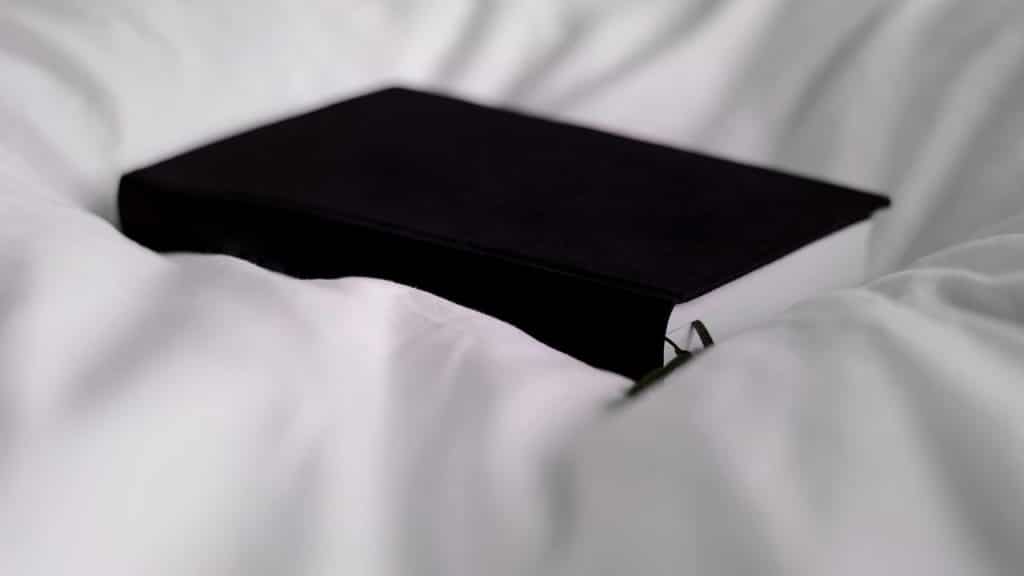 A black hardcover book resting on white bed sheets.