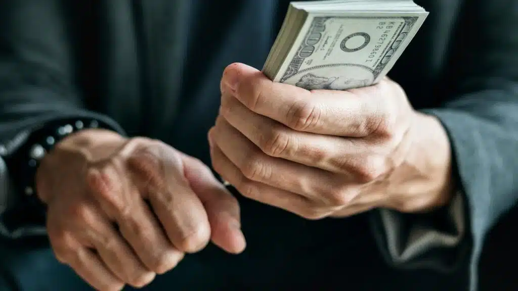 A person holding a thick stack of hundred-dollar bills.