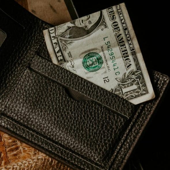 A black leather wallet with a one-dollar bill peeking out.