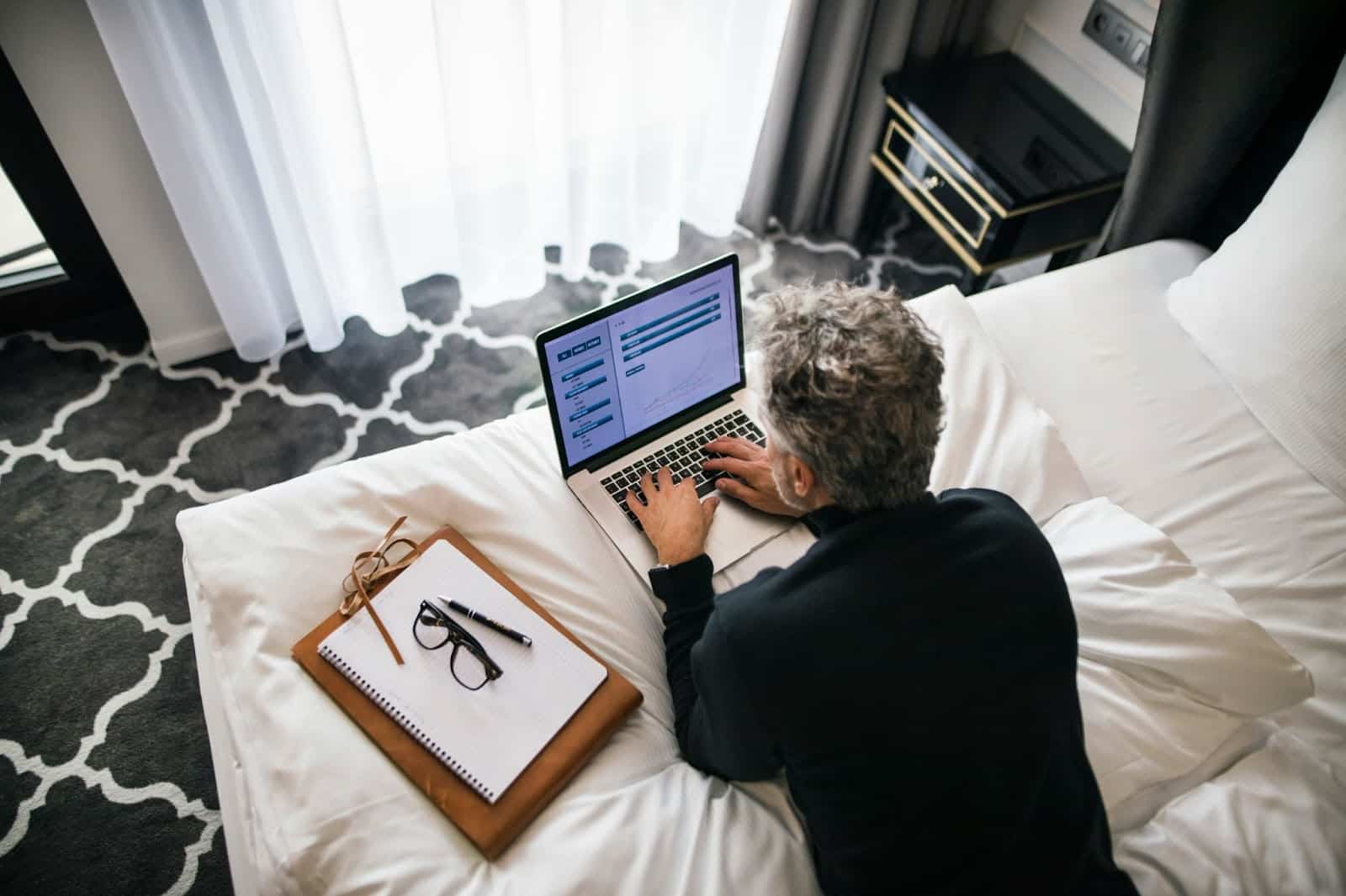 A man checking his laptop while on his bed.