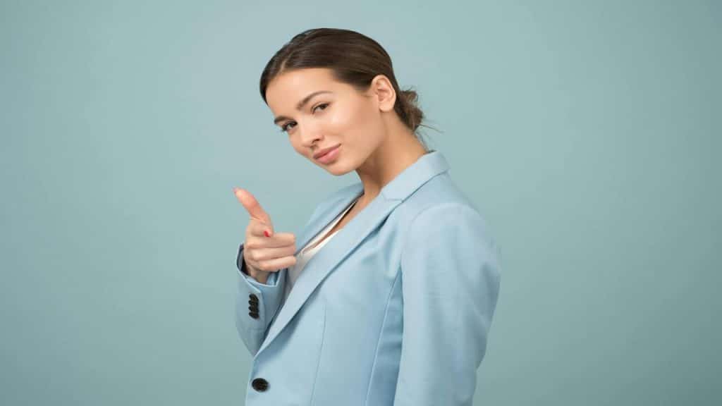 A woman in a blue suit pointing at the camera.