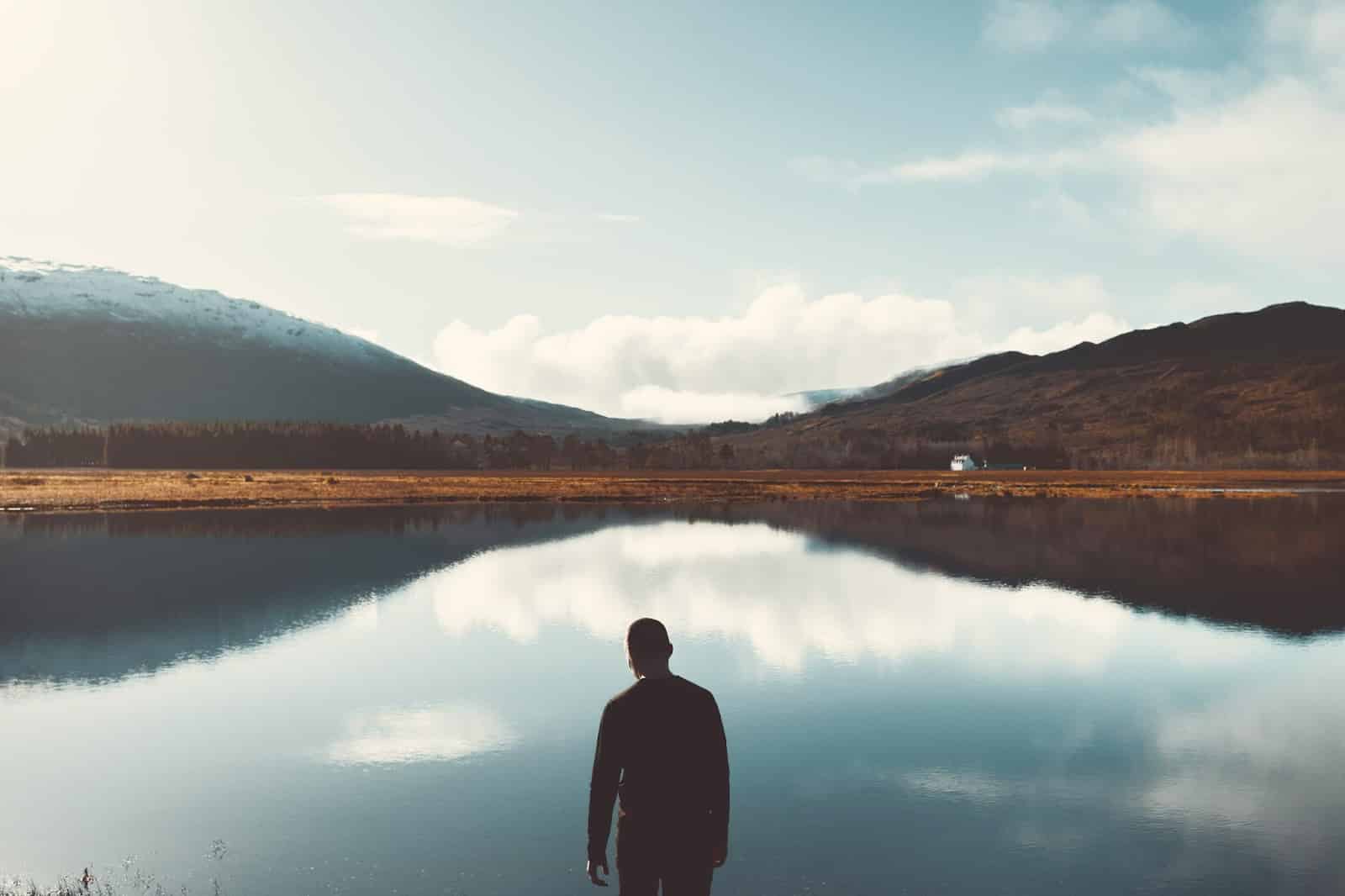 A man standing alone in front of a lake.