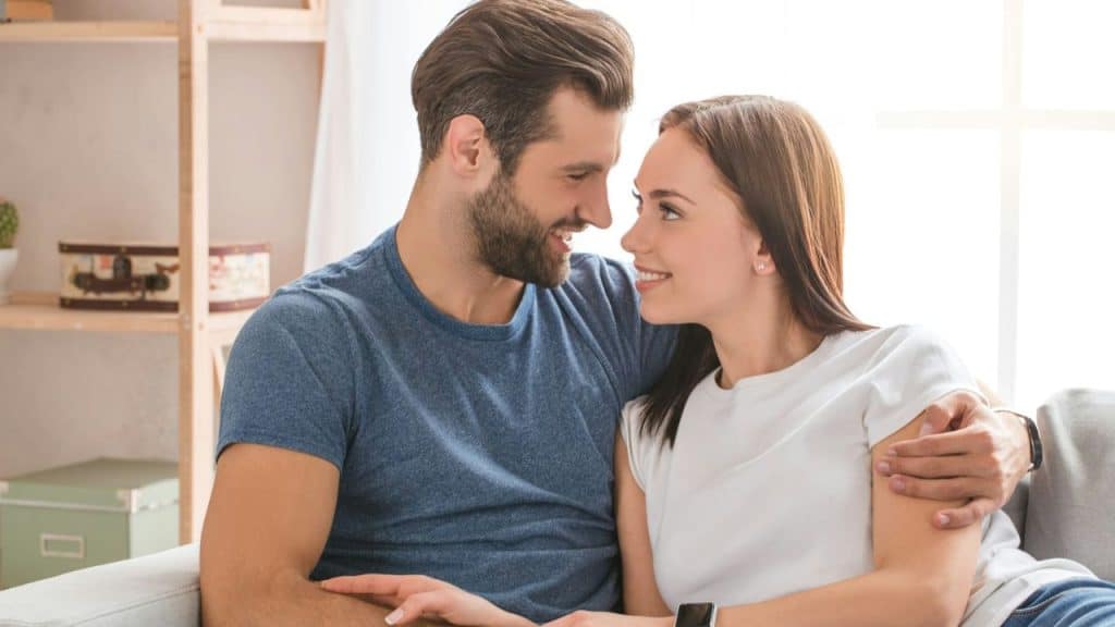 A smiling man and woman gaze at each other, with the man's arm around her.