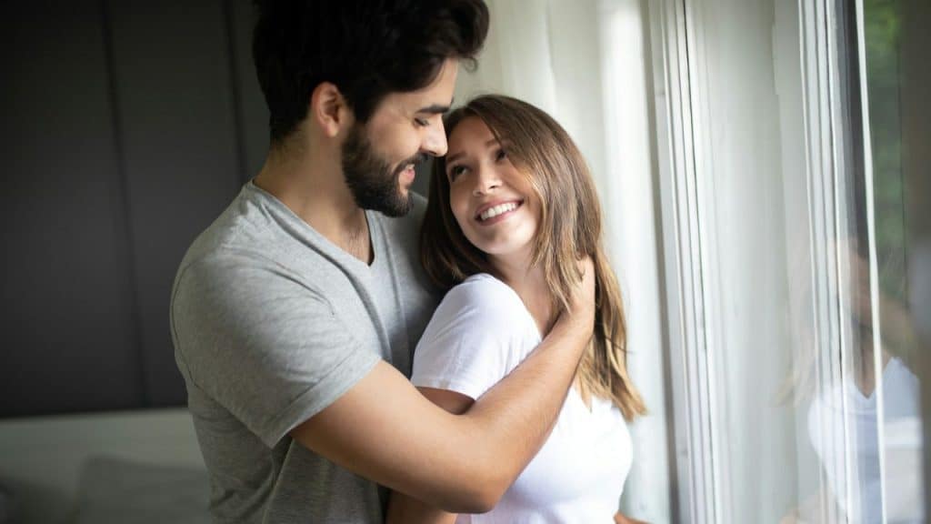 A smiling man and woman with brown hair embrace, looking at each other.