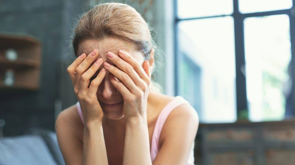 A woman with blonde hair covers her face with her hands, looking distressed.