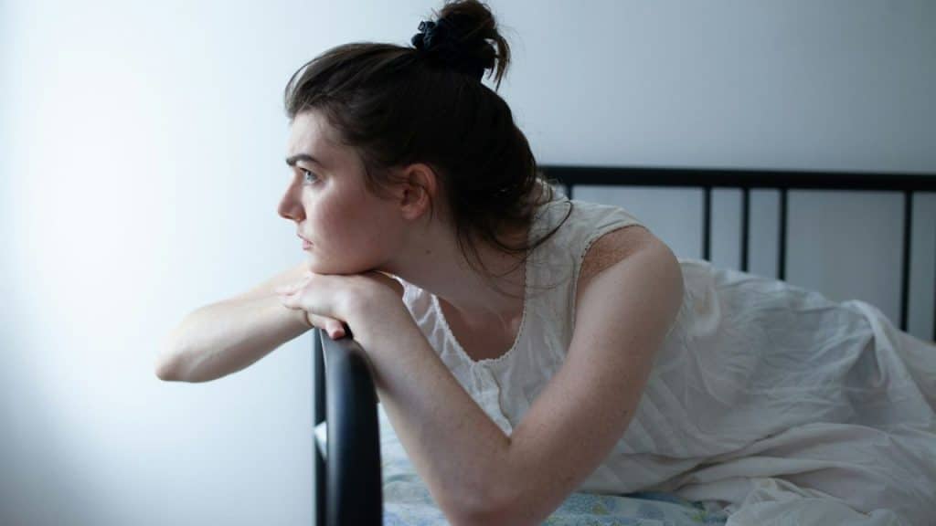 A person with brown hair in a bun rests their chin on their hands while looking out of frame.