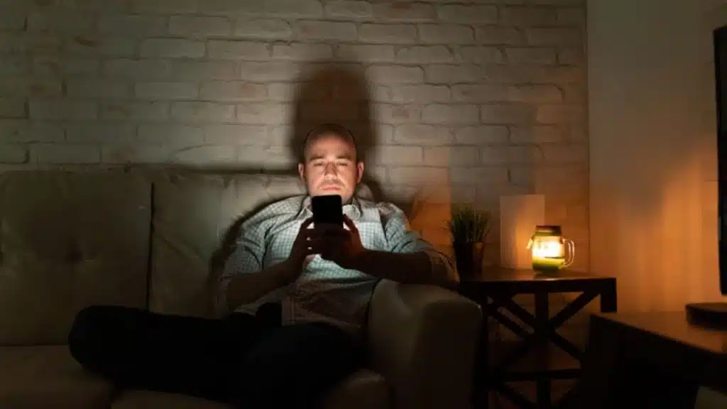 Man sitting alone in a dark room, holding a phone but not texting