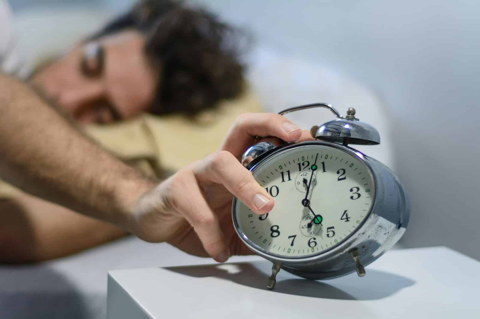 A man turning off his alarm clock.